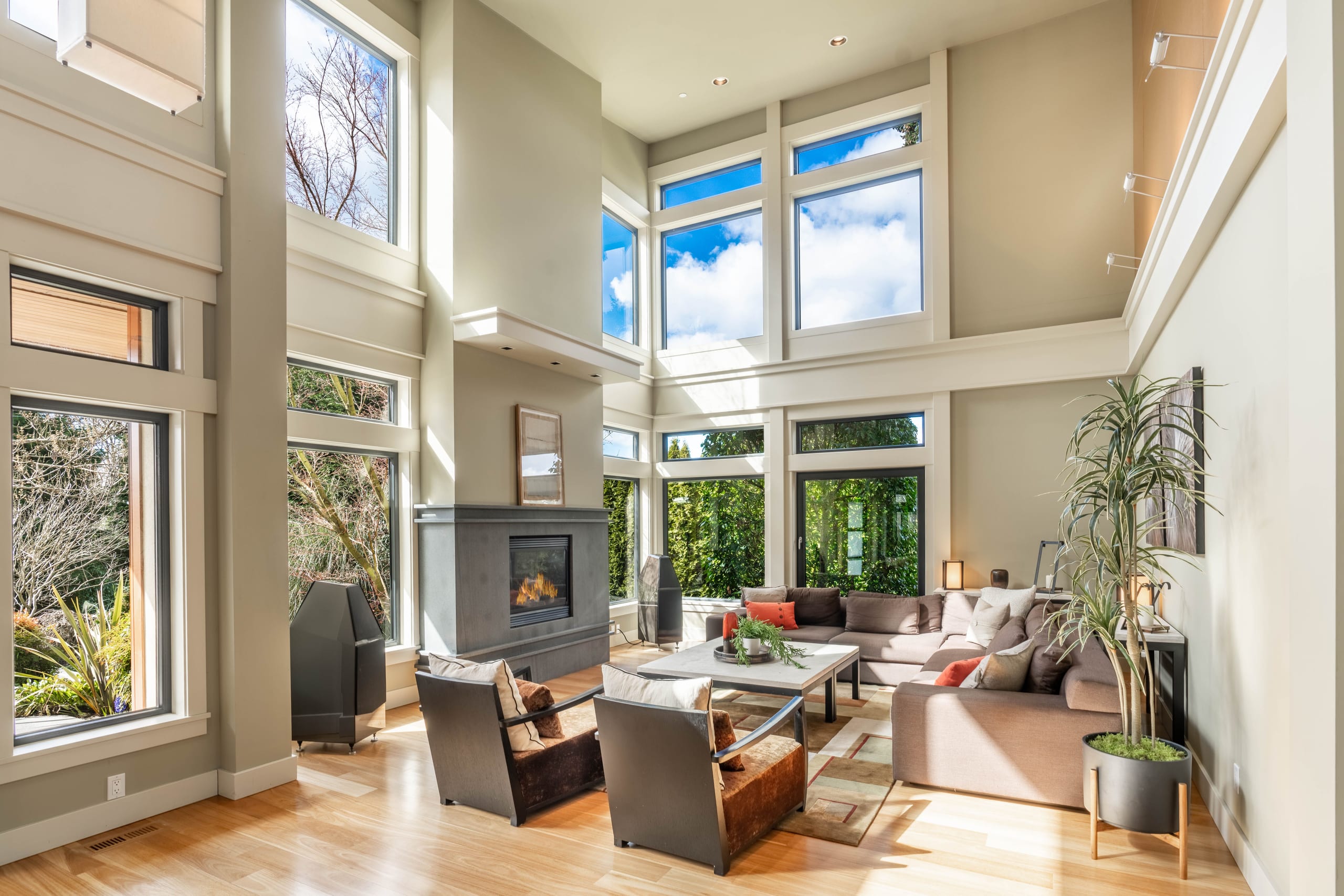 Stunning great room of a luxury home with soaring floor-to-ceiling windows, a fireplace, and warm natural light