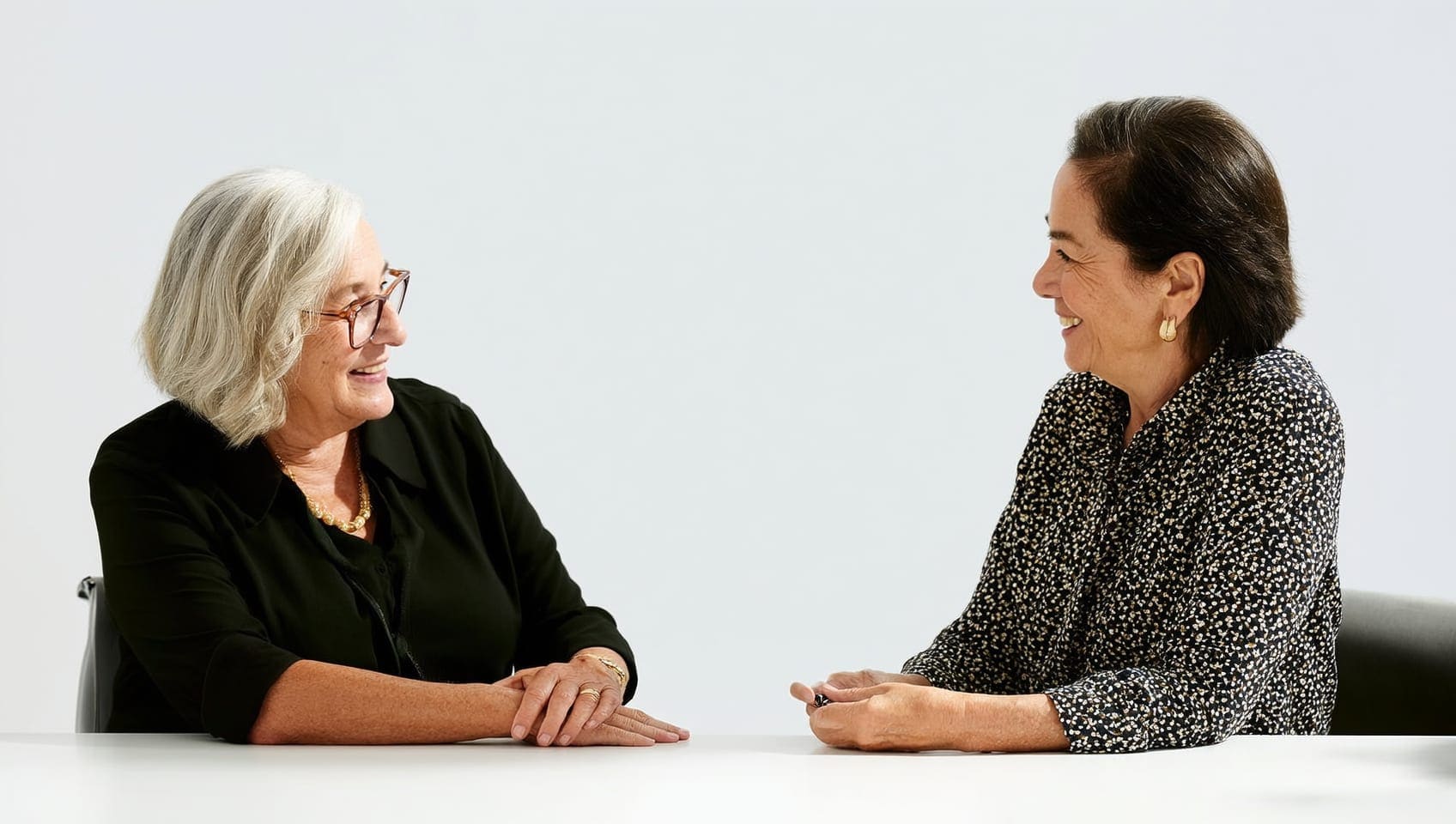 Two JULY Luxury colleagues of different generations in quiet conversation at a bright office table